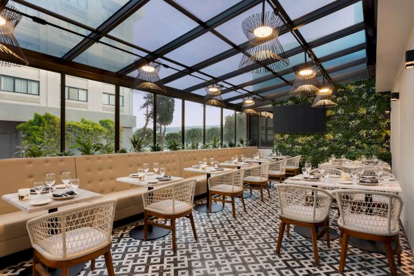 A modern restaurant with a glass roof, patterned floor tiles, and cozy seating arranged with tables set for dining.